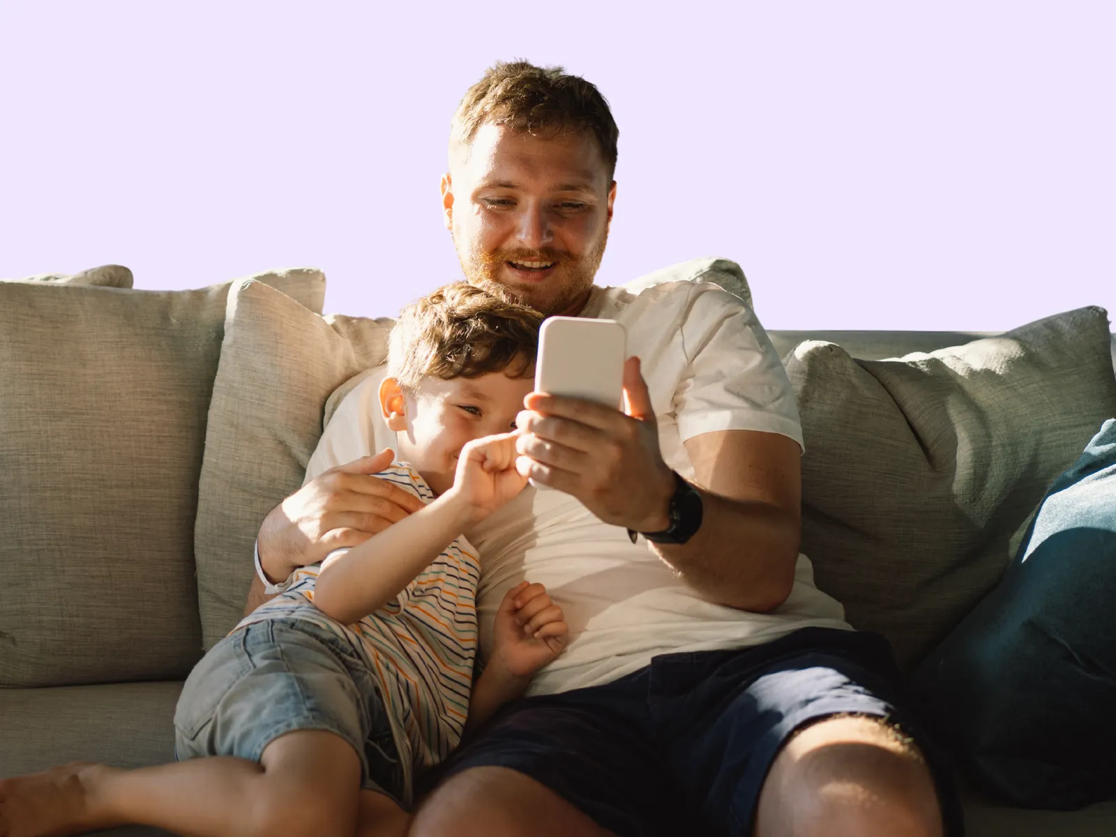 A dad and his young son sitting together on a couch, looking at a phone