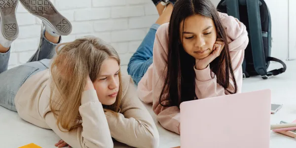 Two girls using a laptop together on a bed